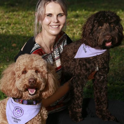 Jess sitting on the grass with two dogs each wearing a scarf
